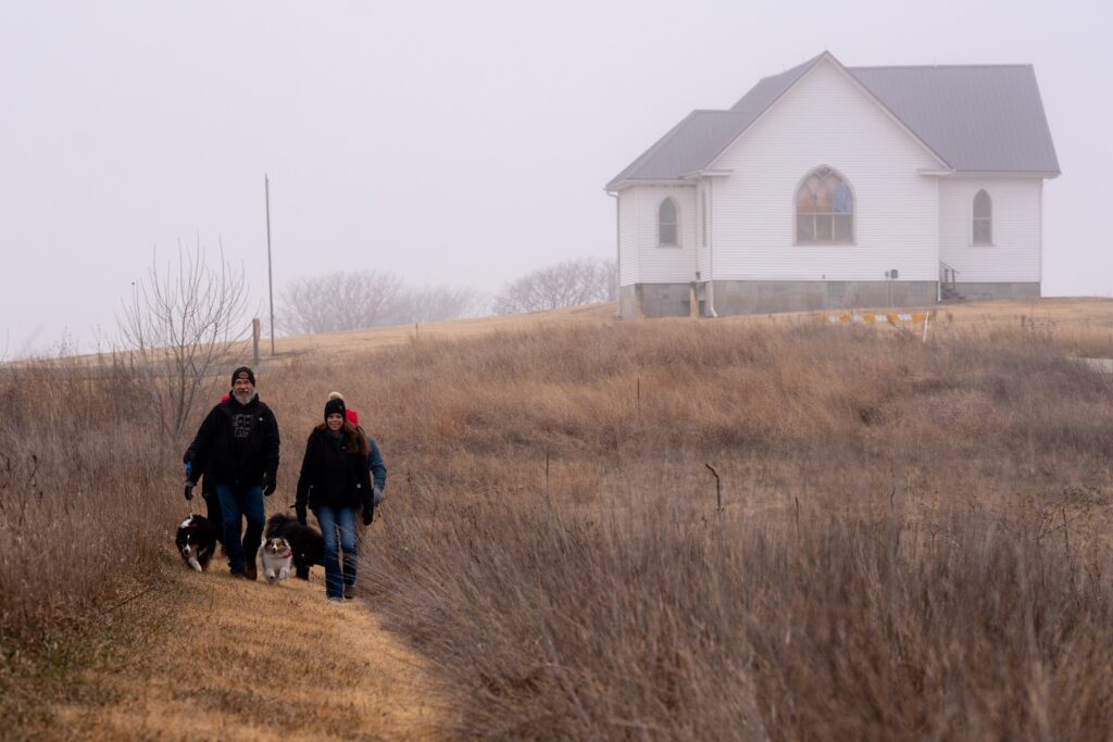 A family with their dogs walking on a lake trail by an abandoned church in the winter.