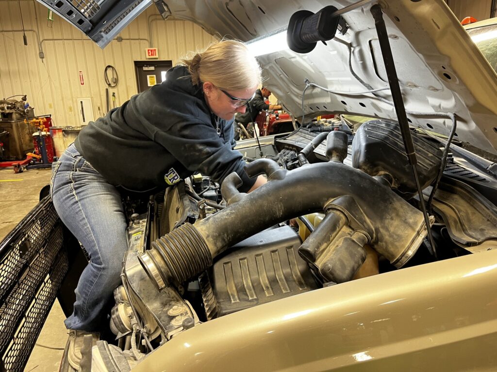 A woman mechanic works under the hood of a truck.