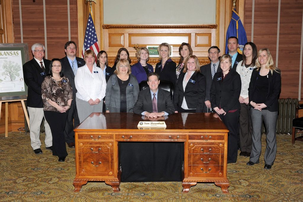 A leadership class gathering around the Kansas Governor for a picture in his office.