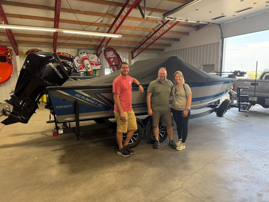 A couple poses in front of a newly purchased boat from a sales man